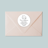 A light pink envelope with a white circular label on it, which contains text and a house illustration.