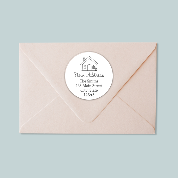 A light pink envelope with a white circular label on it, which contains text and a house illustration.