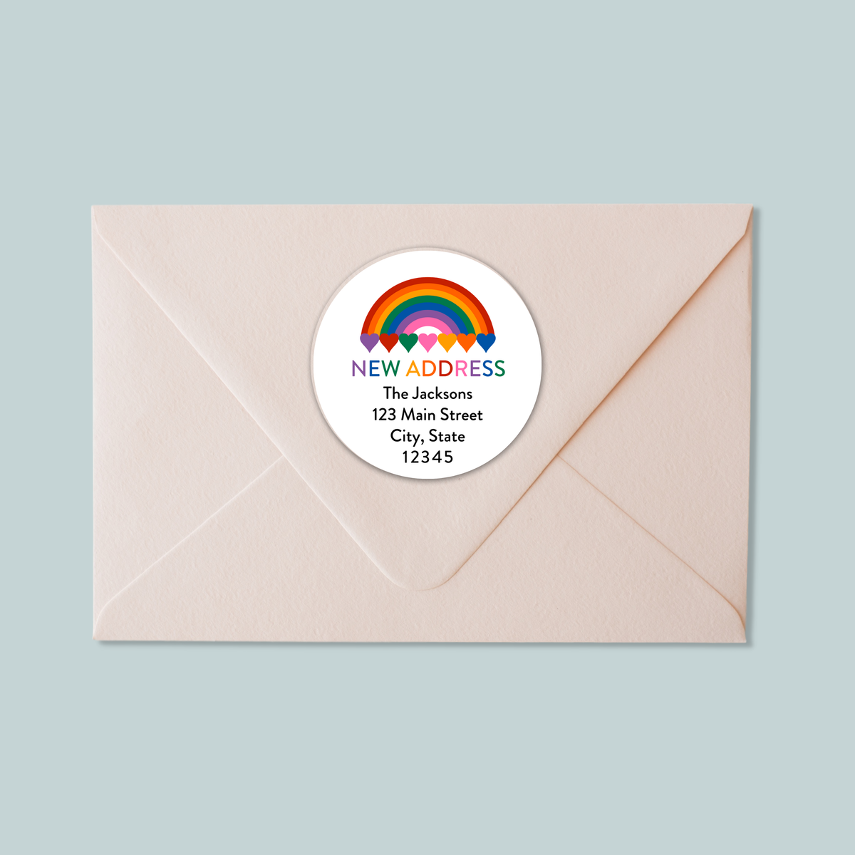 A light pink envelope with a white circular address label featuring a rainbow graphic and text.