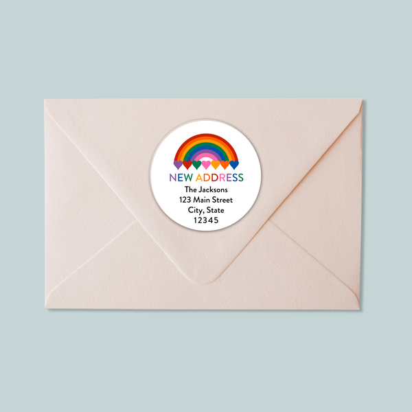 A light pink envelope with a white circular address label featuring a rainbow graphic and text.