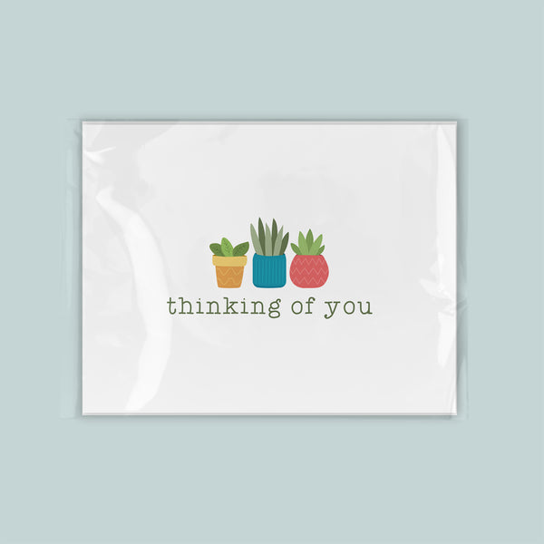 A greeting card with a simple design featuring three potted plants with different colored pots, accompanied by the text "thinking of you".