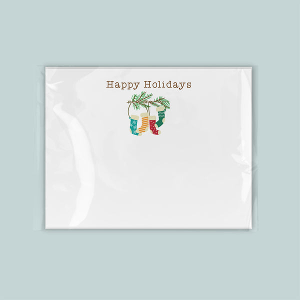 A white greeting card with a festive holiday design featuring a pair of colorful stockings hanging from a branch.