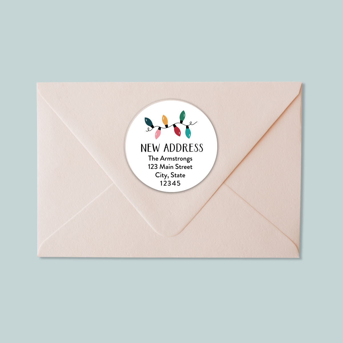 A light pink envelope with a white circular label that reads "NEW ADDRESS The Armstrongs 123 Main Street City, State 12345".