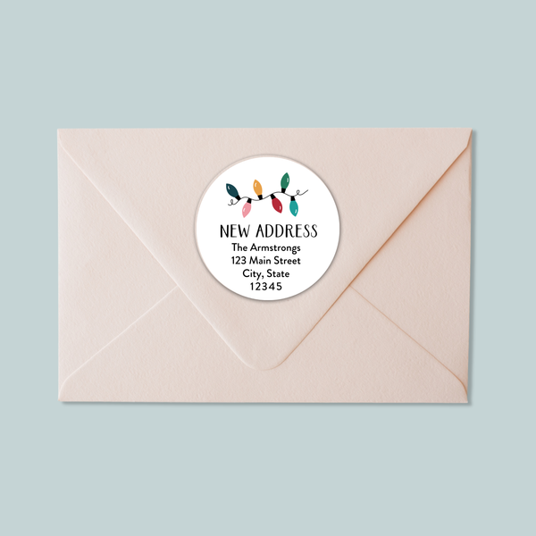 A light pink envelope with a white circular label that reads "NEW ADDRESS The Armstrongs 123 Main Street City, State 12345".