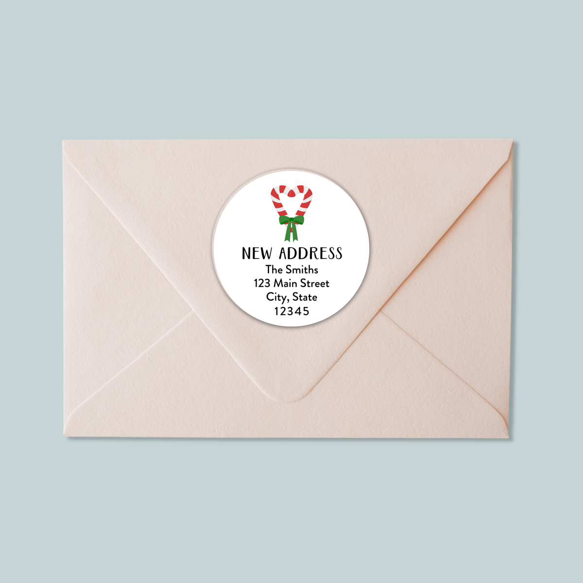 A light pink envelope with a white circular label that reads "NEW ADDRESS The Smiths 123 Main Street City, State 12345".