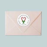 A light pink envelope with a white circular label featuring a red and white striped candy cane design.