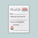 The image is a white thank you card with a pink flower and a stack of books as decorations. The card has a blank space for a message and a blank space for a signature.