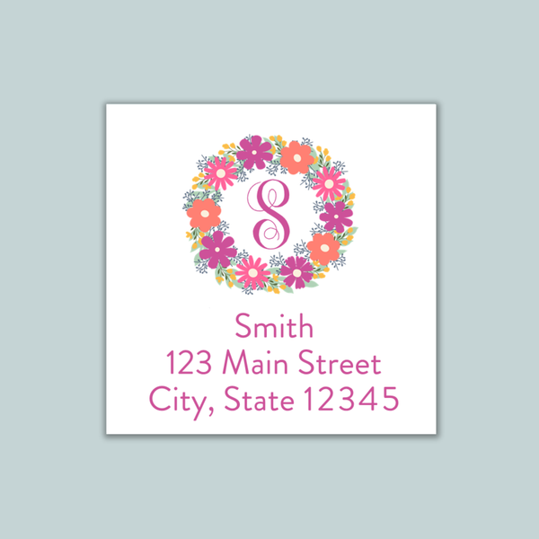 A white square-shaped address label with a floral wreath design and the number 8 in the center. The label includes the text "Smith 123 Main Street City, State 12345" and is set against a light blue background.