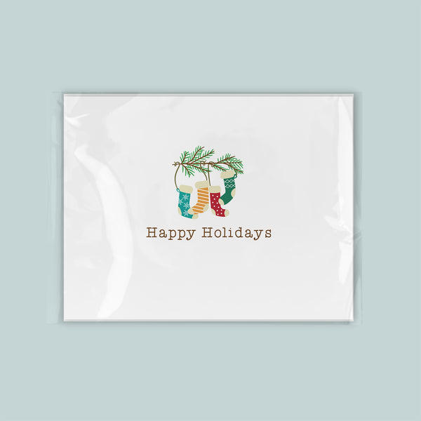 A white greeting card with a festive design featuring colorful Christmas stockings and a pine tree branch.