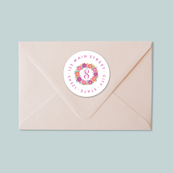 A light pink envelope with a white circular sticker on the flap, displaying a floral design and the number 8.