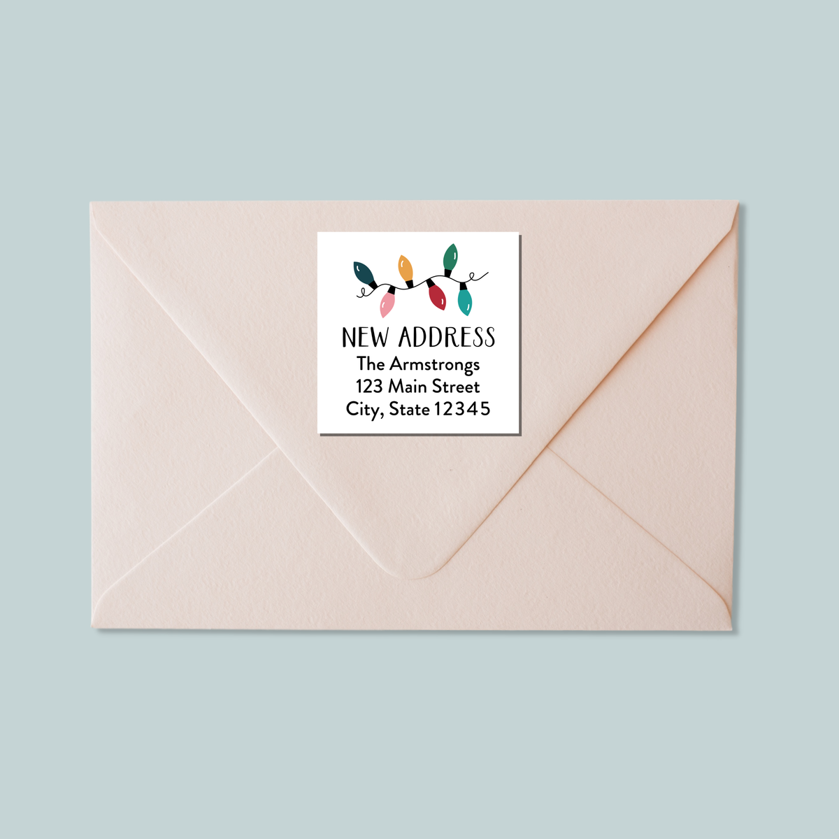 A light pink envelope with a white label that reads "NEW ADDRESS The Armstrons 123 Main Street City, State 12345".