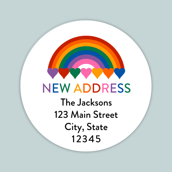 The image is a white circular label with a rainbow graphic and the text "NEW ADDRESS" in the center. Below the rainbow graphic, the text reads "The Jacksons 123 Main Street City, State 12345".