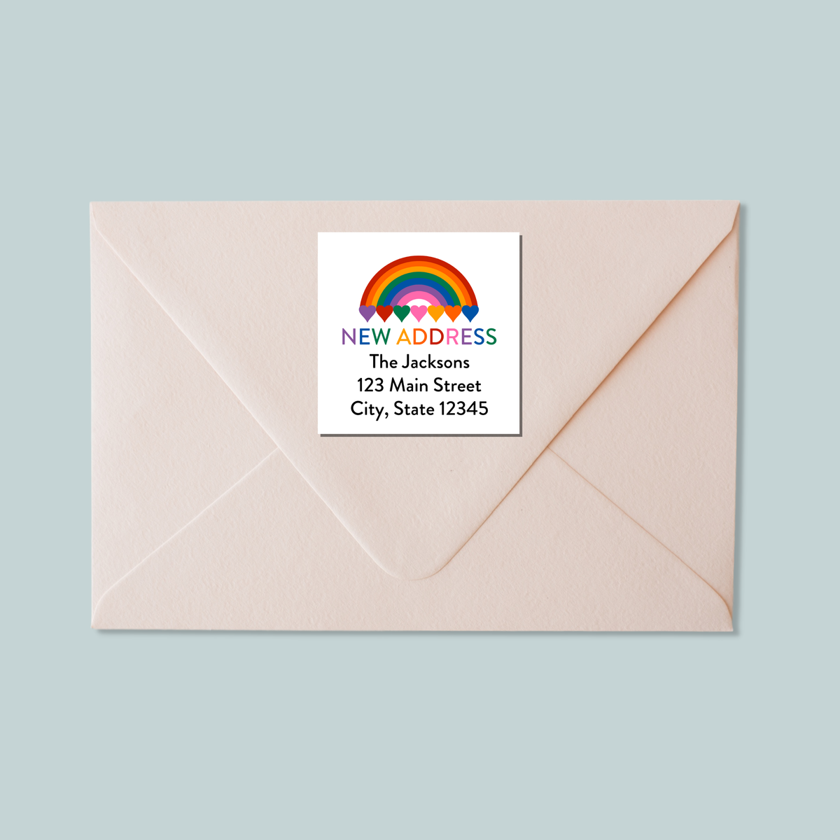 A white envelope with a label that reads "NEW ADDRESS The Johnsons 123 Main Street City, State 12345" and features a rainbow graphic.