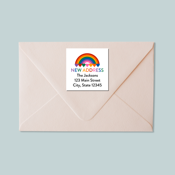 A white envelope with a label that reads "NEW ADDRESS The Johnsons 123 Main Street City, State 12345" and features a rainbow graphic.
